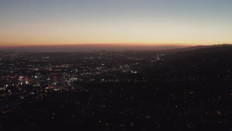 Antena:-Vista-De-180-Grados-Sobre-Las-Colinas-De-Hollywood-Por-La-Noche-Con-Vista-Al-Centro-De-Los-Ángeles,-Luces-De-La-Ciudad