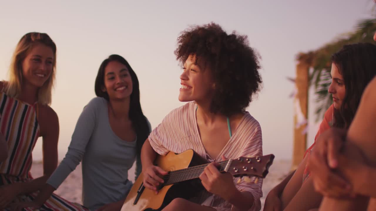 Donna di etnia mista che suona la chitarra per i suoi amici sulla spiaggia