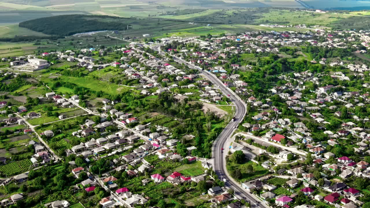 Aerial drone view of a village and road with cars, greenery, hills, Moldova