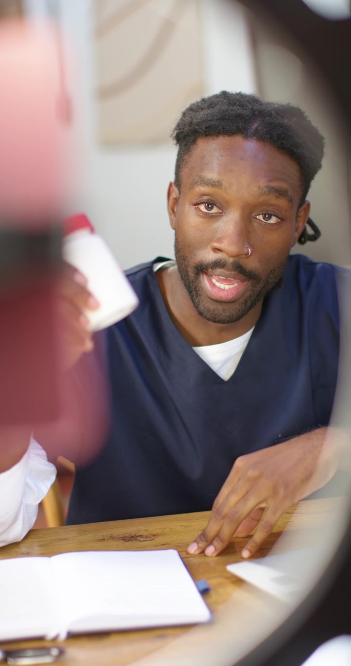 Vertical video: African American man consulting, showing pill bottle with red cap, noting dosage