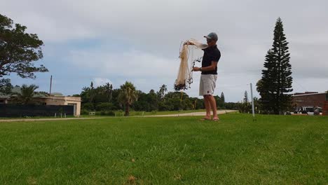 un hombre practicando cómo lanzar una red de enmalle sobre un césped en un día soleado