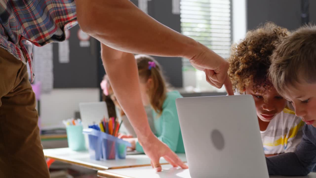 vista lateral del maestro caucásico que enseña a los escolares en la computadora portátil en el aula 4k