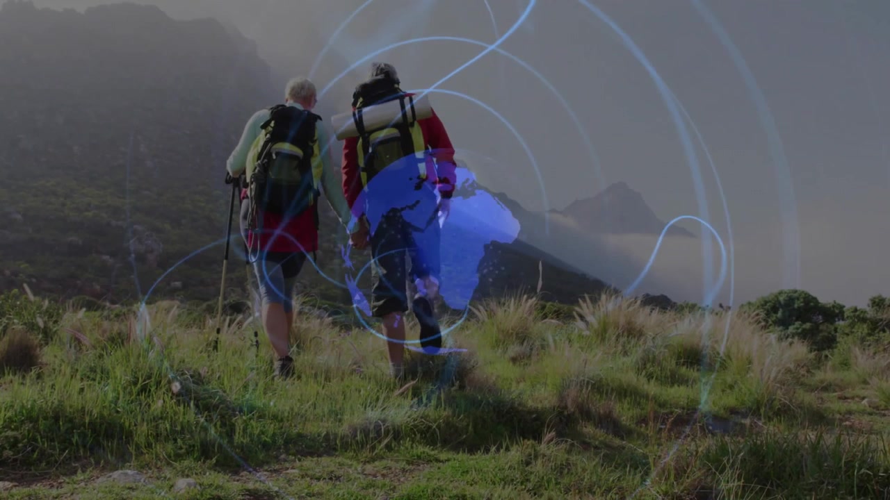 Coppia in escursione che si tiene per mano su una collina costiera, camminando in salita, con anelli tecnologici blu che formano un globo rotante.