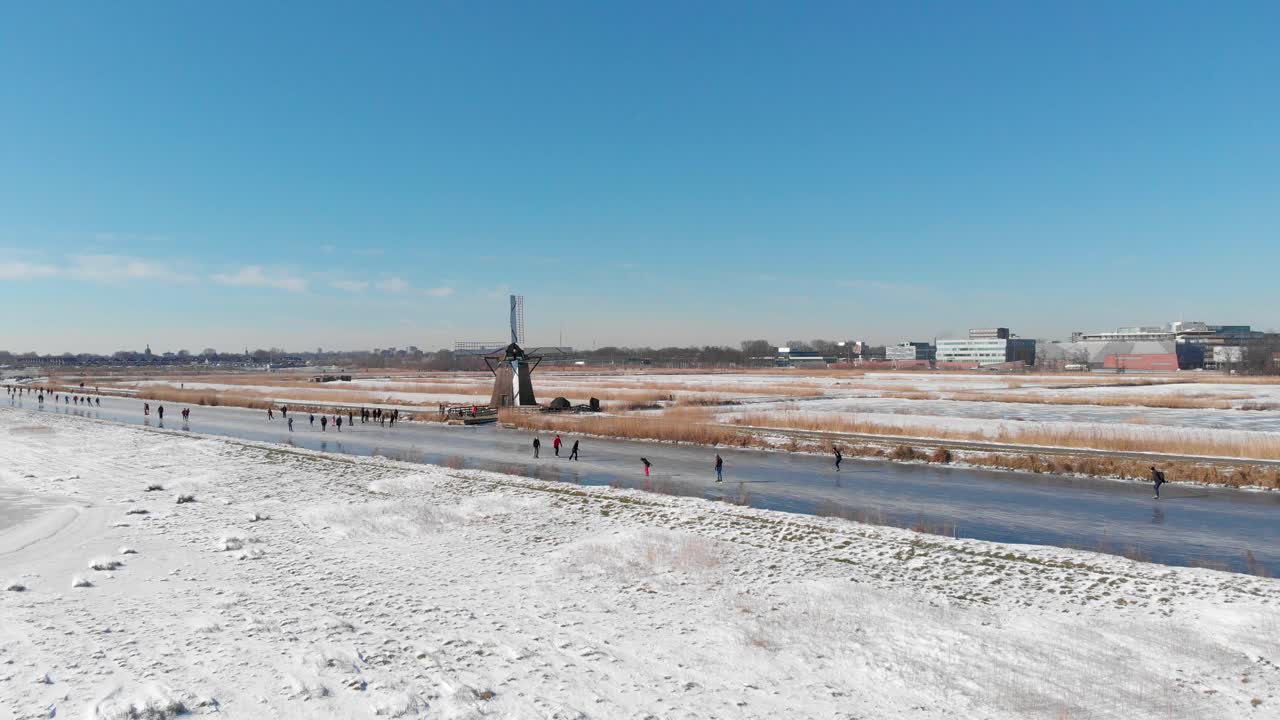 Dutch locals ice skating on frozen canals near old windmill, winter aerial view