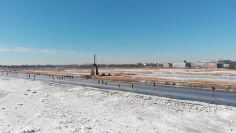 dutch locals ice skating on frozen canals near old windmill, winter aerial view