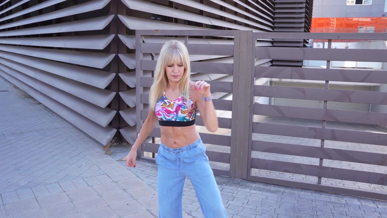 Elegante donna bionda in abbigliamento sportivo in posa vicino a una struttura moderna in un contesto urbano colorato.