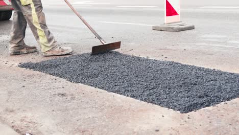 trabajador de la construcción está distribuyendo asfalto nuevo vertido en la carretera y lo prepara para ser comprimido