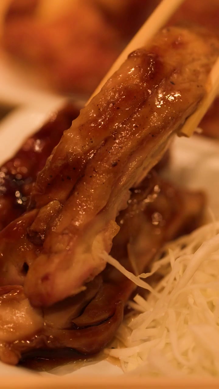Plano detalhe de pauzinhos levantando um pedaço de frango teriyaki glaceado em um restaurante