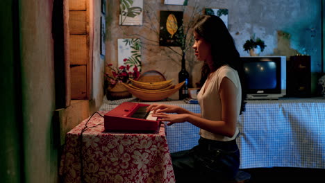 chica asiática tocando el teclado en casa, vista lateral estática
