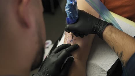 a close-up of a tattoo artist makes a tattoo on a woman's arm. a high resolution. professional tattooist works in studio. high angle footage from the shoulder of master