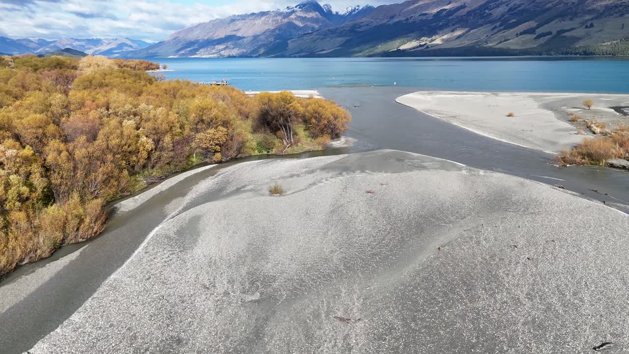 Drone footage captures a tranquil river winding through vibrant autumn foliage under clear skies, showcasing natural beauty and calmness