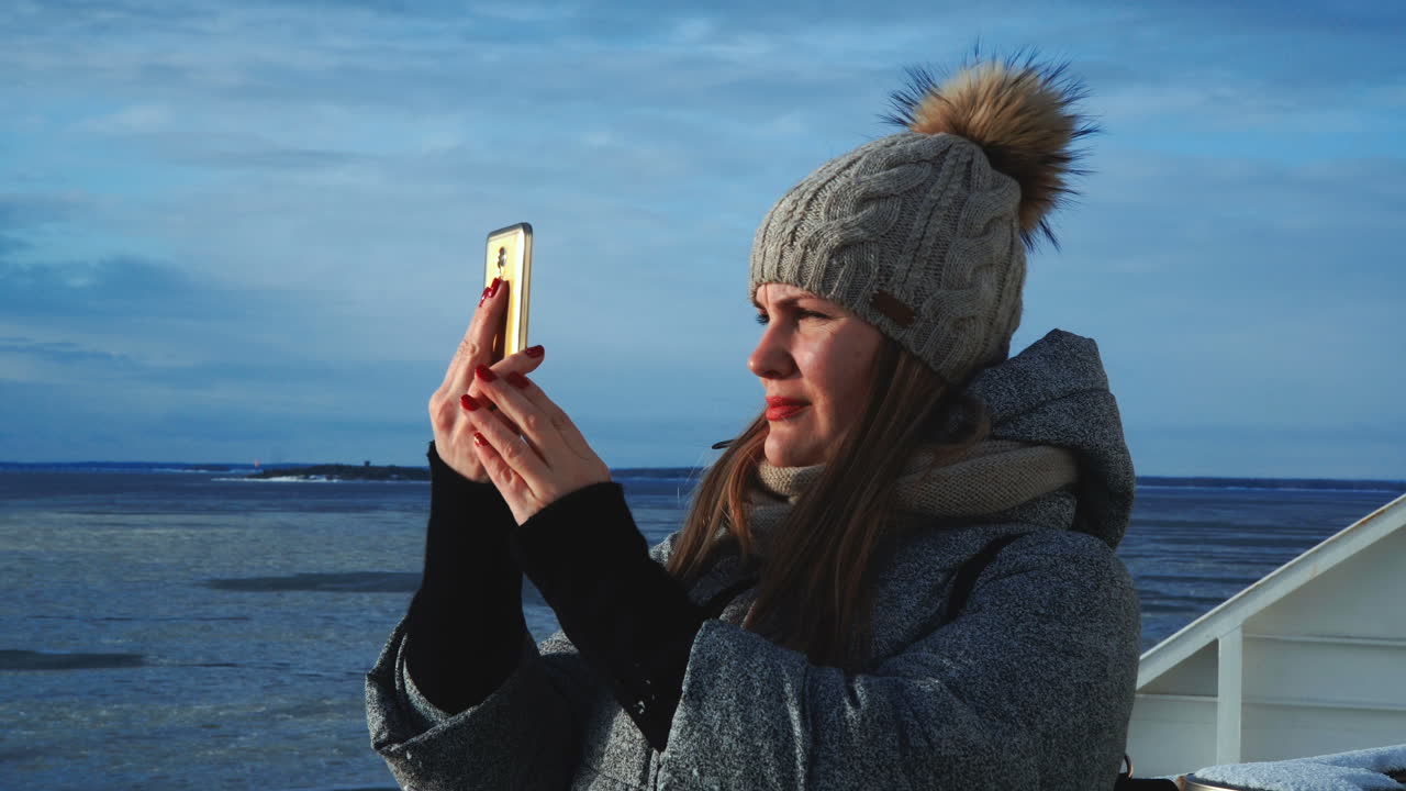 Woman taking a photo of an icy winter landscape with her smartphone