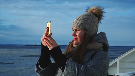 woman taking a photo of an icy winter landscape with her smartphone