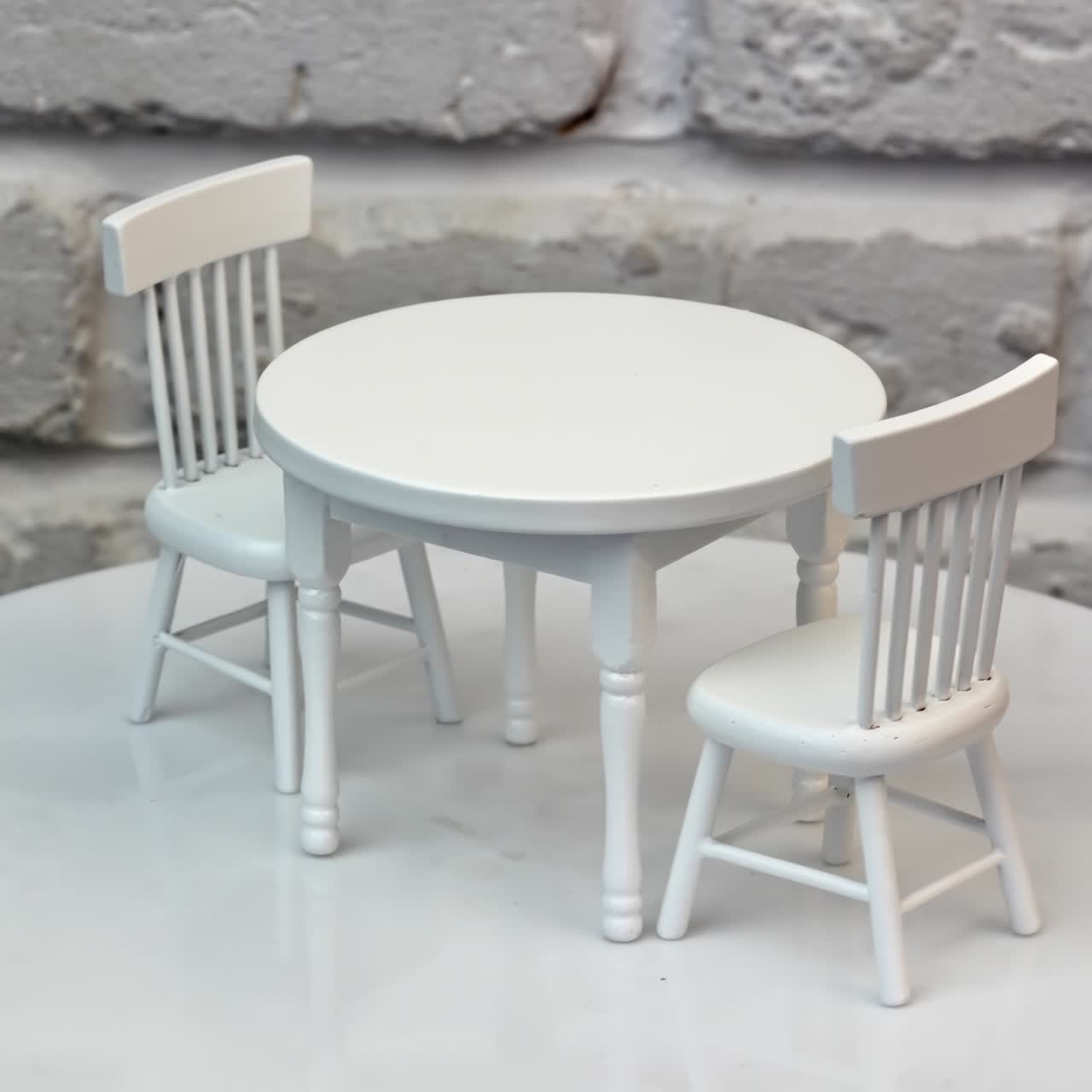 Toy round table and two little chairs beside. Beautiful pieces of dolly furniture at rotating table. White wall background