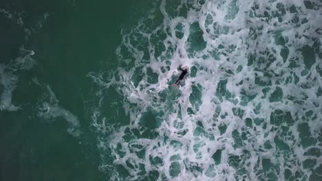 birds-eye-view of surfer duck-diving choppy waves. drone-shot