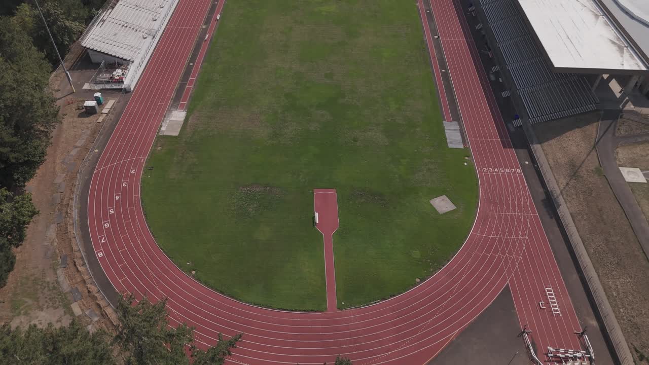 Weite Drohnenaufnahme, die sich durch Bäume bewegt, um die Tribünen eines College-Stadions und Leichtathletikanlagen zu enthüllen.