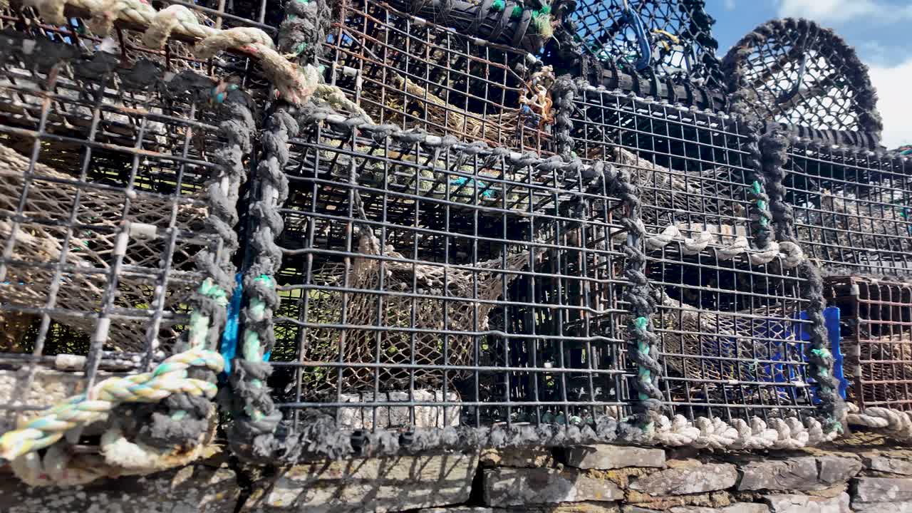Trappole per granchi e nasse per aragoste impilate su un muro di pietra sotto un cielo blu. Panoramica a sinistra