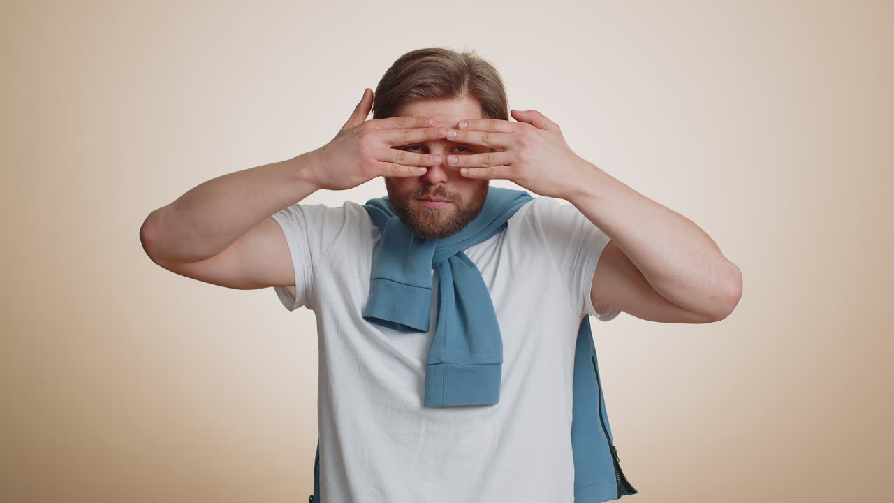 Curious caucasian man closing eyes with hand and spying through fingers hiding and peeping