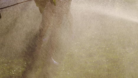 Two-barefoot-women-run-on-the-green-grass-in-jets-of-water.-Youth-and-health-concept