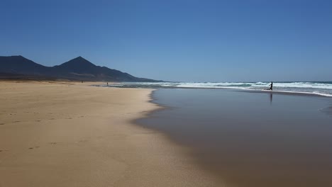 serene view of the immense and remote cofete beach in fuerteventura, with wet sand creating beautiful reflections of the sky and the jandia mountains in the background, spain