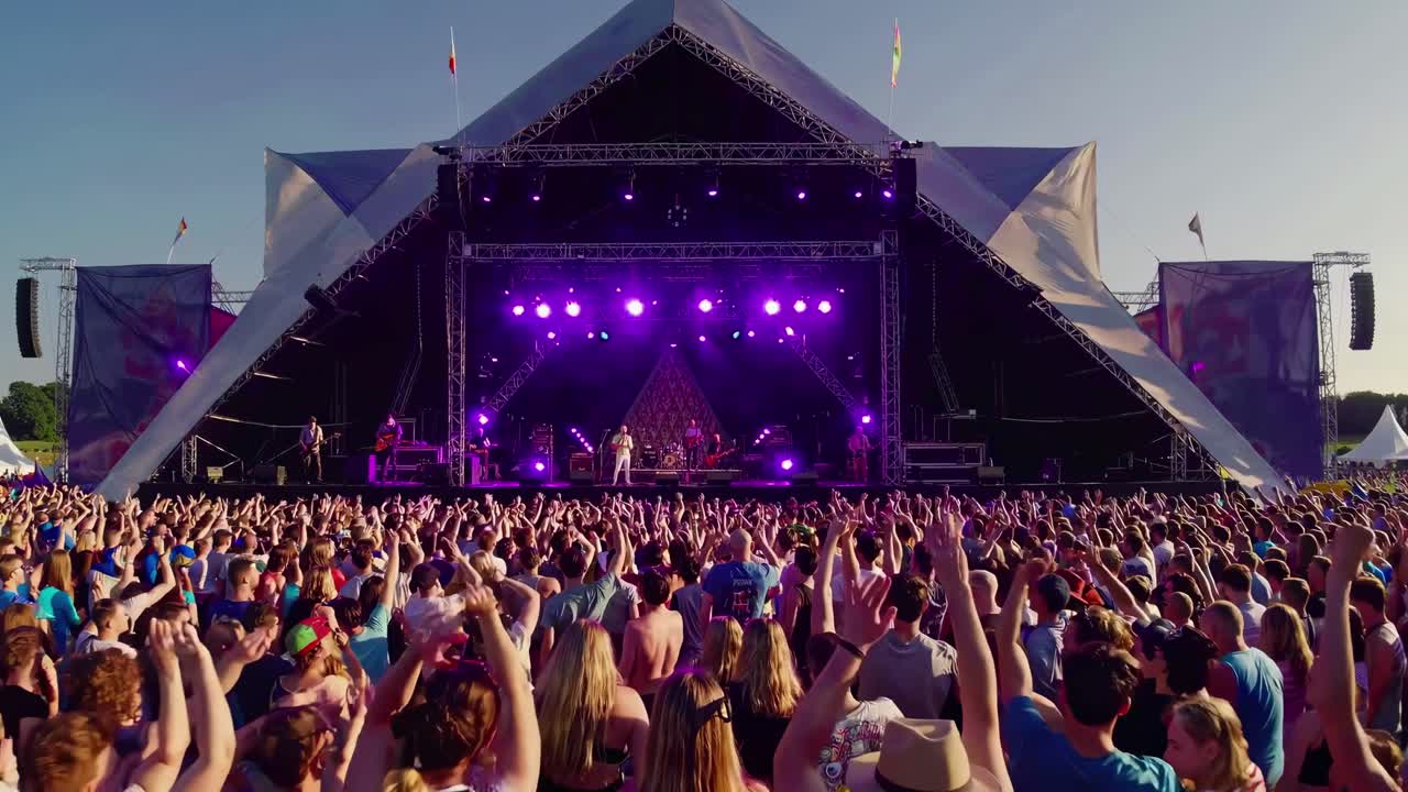 Vidvinkeloptagelse af en livlig udendørs musikfestival, der fanger et festligt publikum og scene.