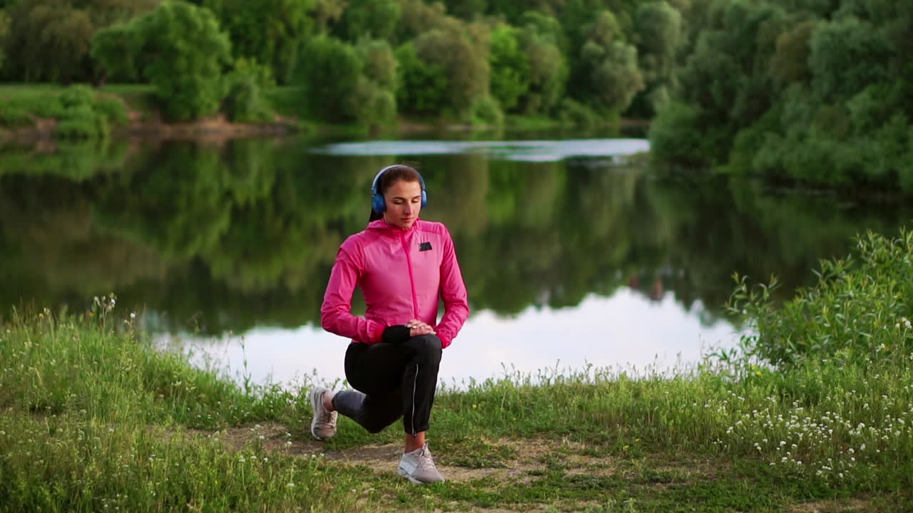 una chica con una chaqueta rosa se está preparando para una carrera de calentamiento y escuchar música en auriculares a través del teléfono