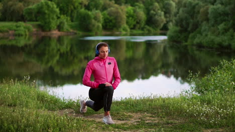 a girl in a pink jacket is preparing for a run warm up and listen to music in headphones through the phone