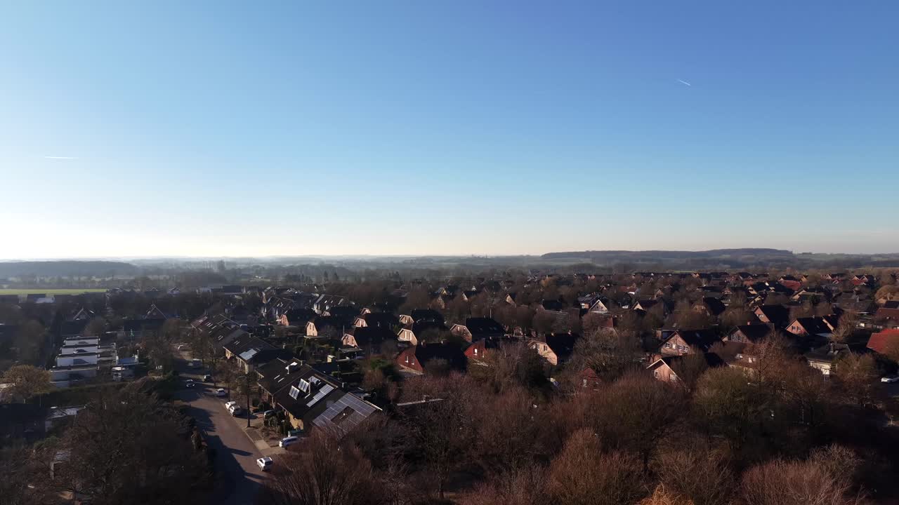 Winterlicher Luftbildflug über ruhige amerikanische Vororte mit roten Backsteinhäusern, kahlen Bäumen und sanftem Sonnenlicht. Ruhige Wohnlandschaft unter klarem Himmel im Dezember. Solarmodule auf den Dächern der Häuser. Weitwinkelaufnahme