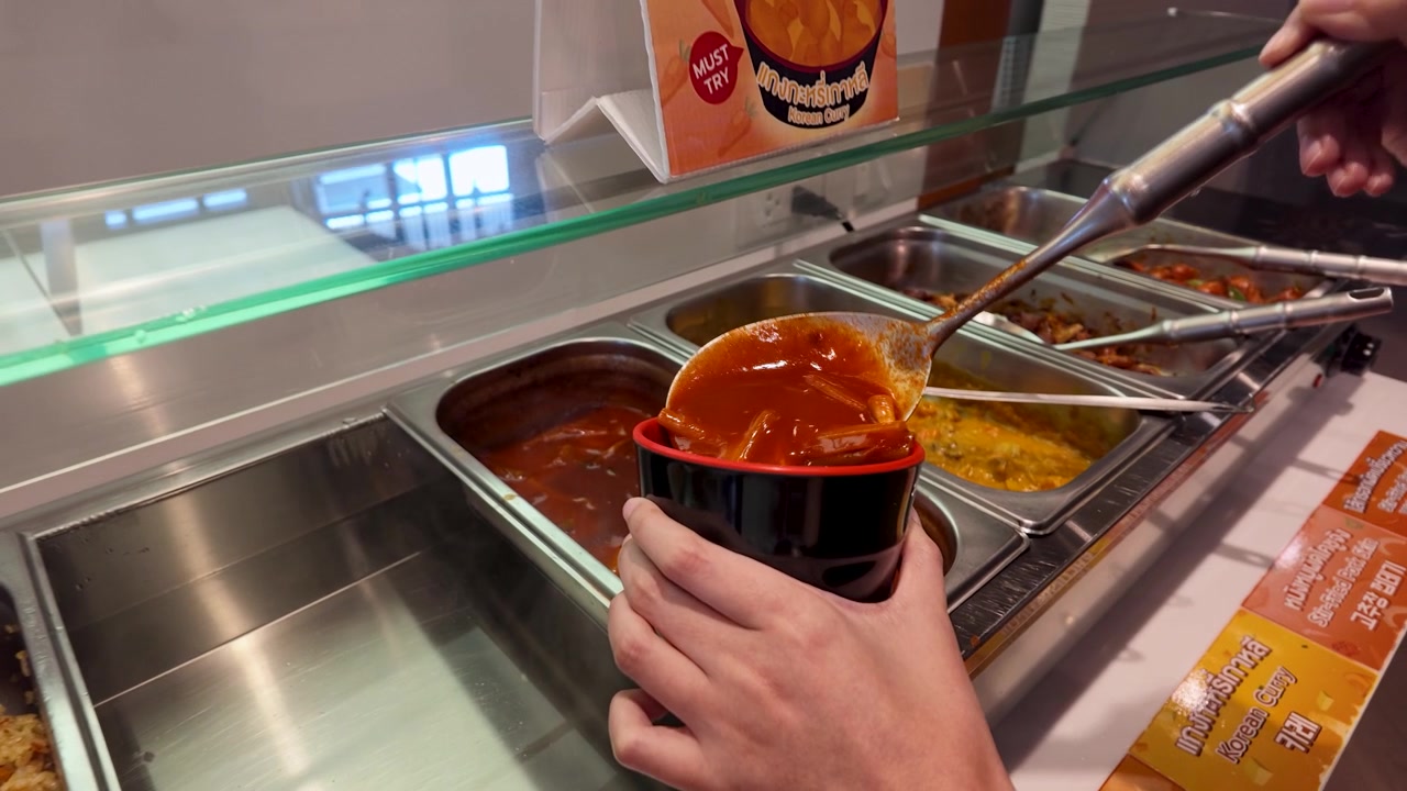 Un mestolo di metallo raccoglie salsa rossa piccante e gnocchi di riso in una ciotola nera.