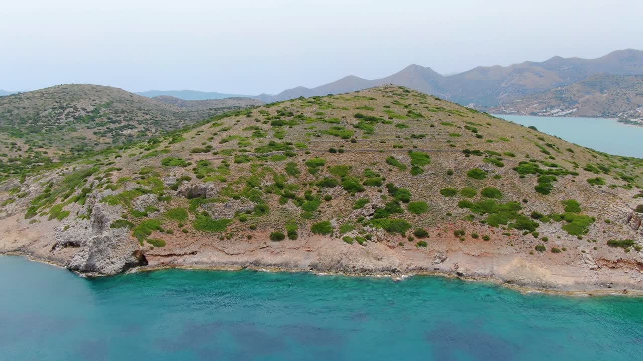 Blue water, arid hill and landscape, Island of Spinalonga, Crete, Greece, aerial pull back