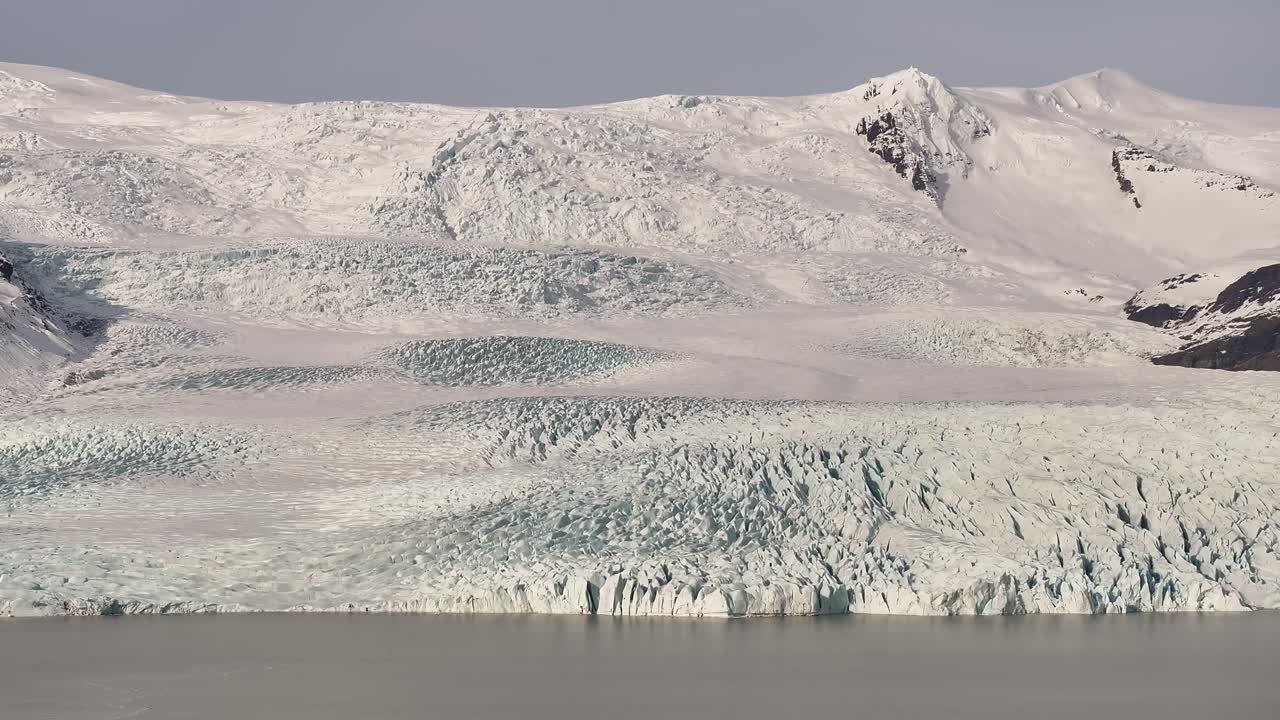 Drone view of Fjallsárlón glacier lagoon in Vatnajökull National Park, Iceland, showcasing ice formations, snowy mountains, and serene arctic landscape.