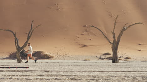 hombre caminando en deadvlei con camelthorn muertos y altas dunas rojas en el fondo