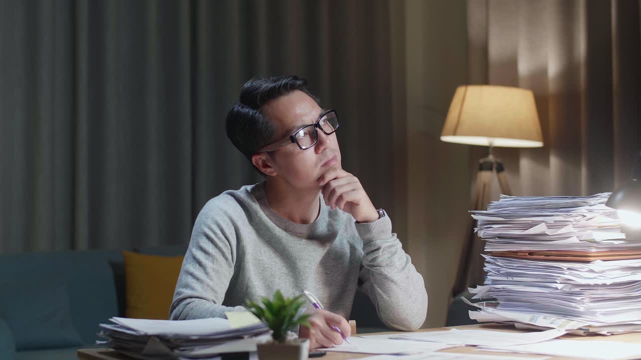 Asian Man Thinking And Looking At Paper Then Raising Index Finger While Working With Documents At Home