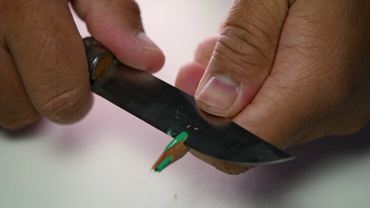 Footage of hands slowly sharpening a pencil and some coloured pencils with a sharp knife