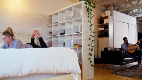 man playing guitar while woman relaxing on bed