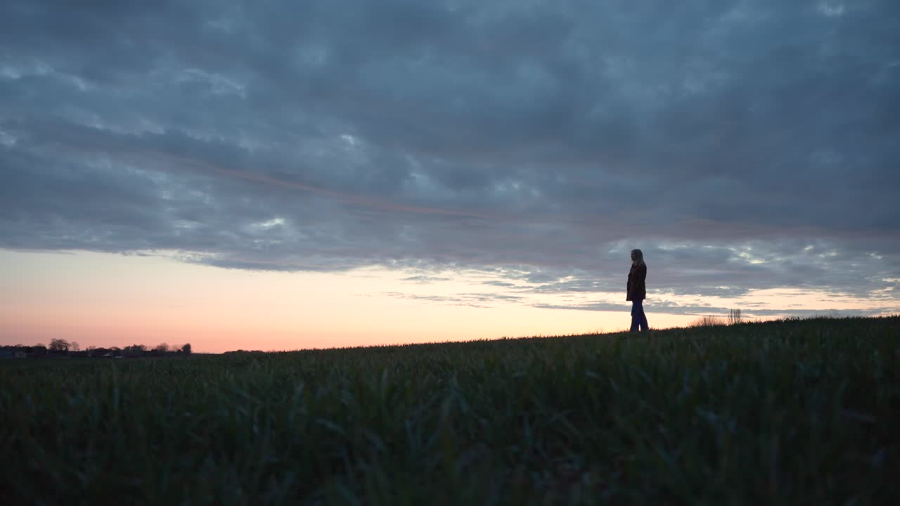 niña de pie en un campo mirando a lo lejos al atardecer