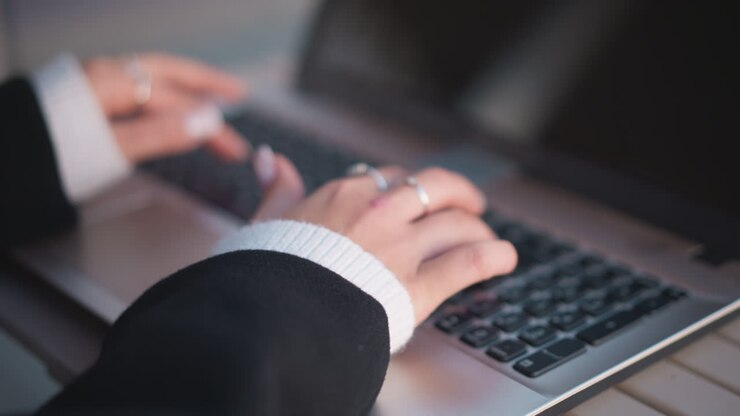 Close-up of hands adorned with polished nails and delicate rings typing on laptop keyboard with slight blur and soft light reflection on screen