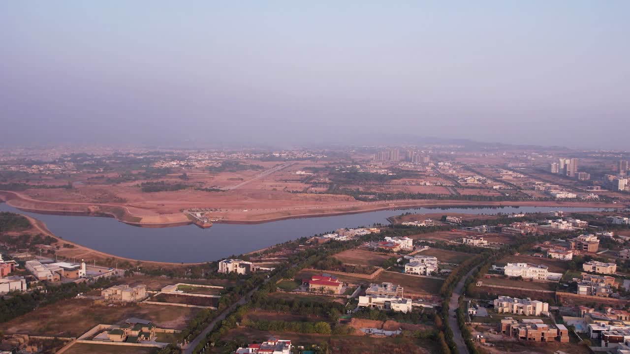 Cuplikan drone di atas daerah pinggiran kota Islamabad dengan sungai yang berkelok-kelok, area perumahan, dan kaki langit yang jauh. Islamabad, Pakistan