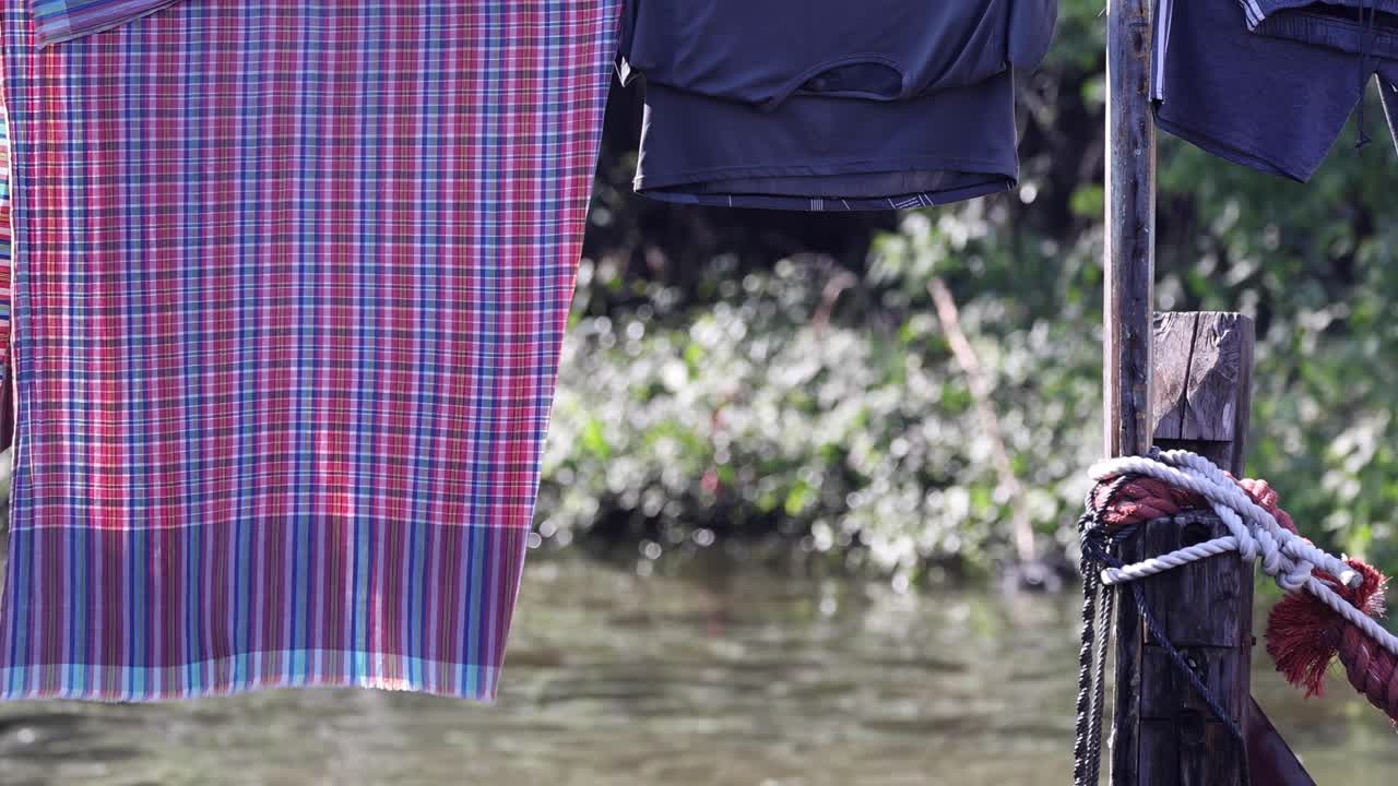 A plaid cloth and dark garment drying on a line near a riverbank.