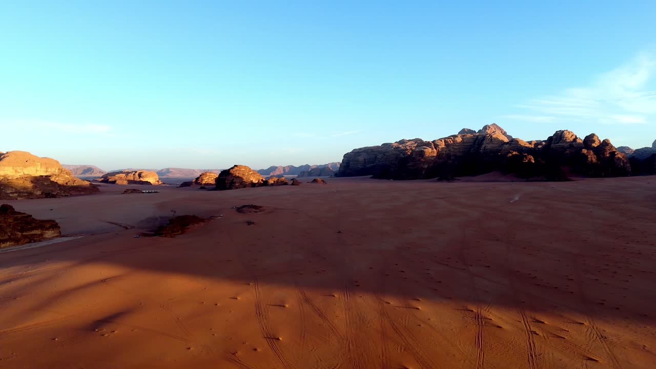 Sequenza aerea con drone che sorvola le valli di sabbia rossa di Wadi Rum mentre il sole tramonta, proiettando lunghe ombre sulle formazioni rocciose