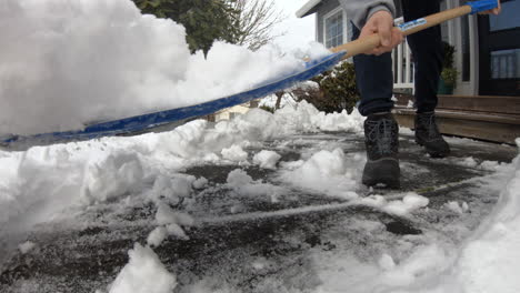 man using a blue snow shovel to clear the snow in front of his porch