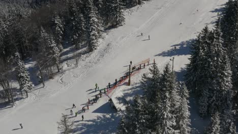 skiers gather at a track in kope resort slovenia in the pohorje mountains, aerial tilt up shot