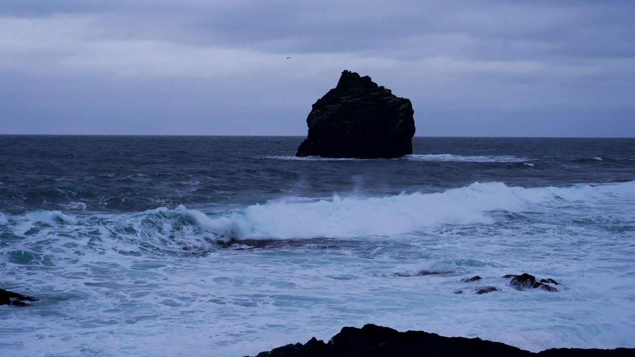 amplia toma de olas que llegan a la costa y karlinn el hombre un alto acantilado, un tapón volcánico erosionado en la costa de valahnúkur, islandia