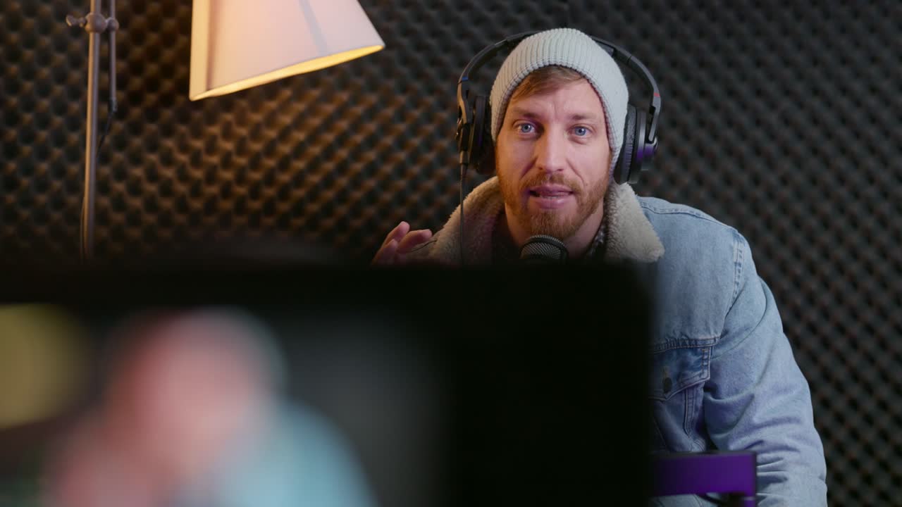 Hipster looking influencer talking to camera in live session in home studio. Professional vlogger or podcaster speaking to audience streaming and recording video. Confident with headphones and mic
