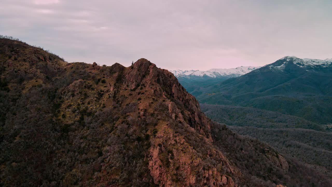Backward drone aerial of rugged mountain ridge at sunset, Ñuble Region, Chile with snow-capped Andes peaks and dramatic twilight sky