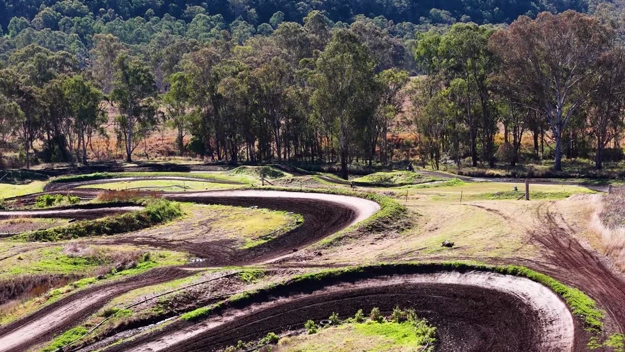 Single motorcyclist navigates winding dirt track, natural daylight, wide shot, rural outdoor setting