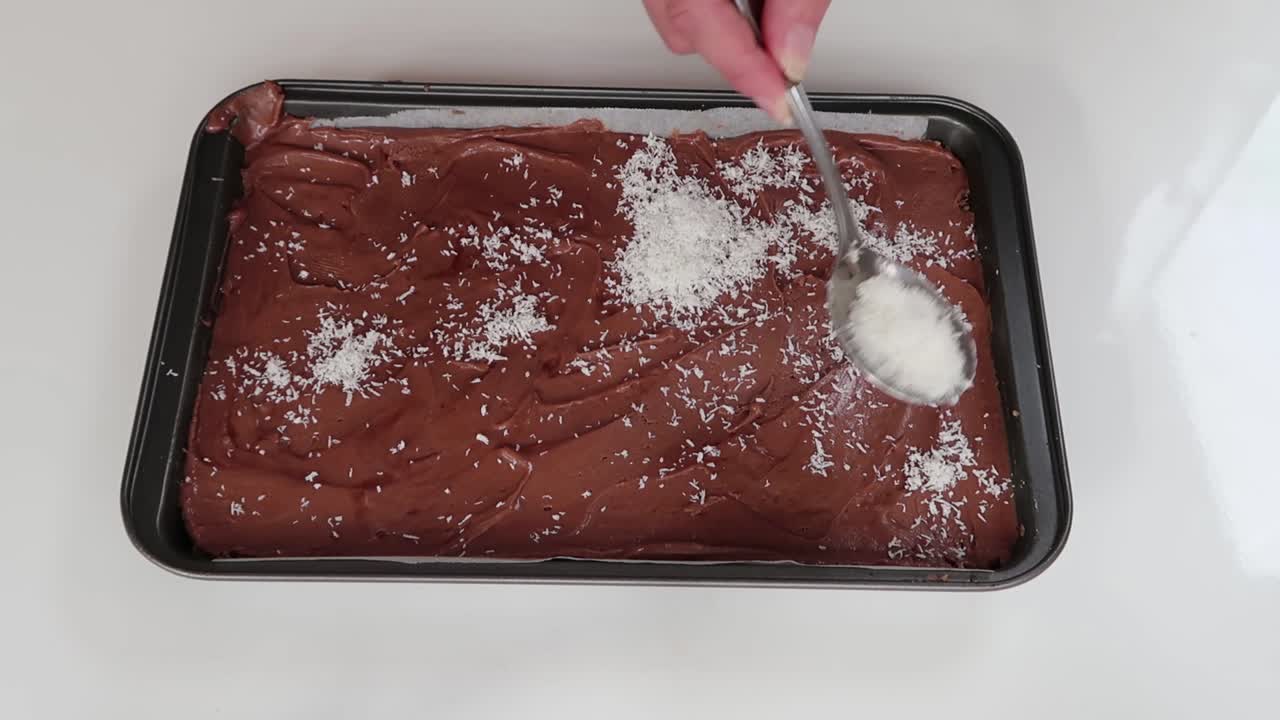 Spreading coconut shavings on a caramel and chocolate slice
