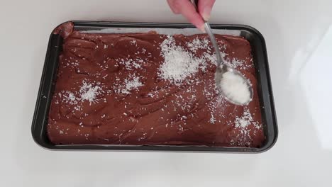 spreading coconut shavings on a caramel and chocolate slice