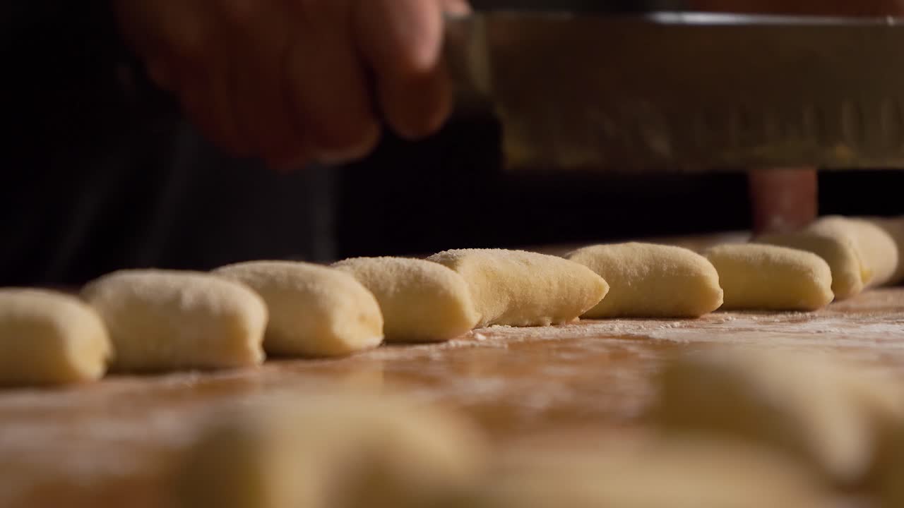 4K Close up slow motion shot home made gnocchi cutted from raw dough roll with knife on a wooden table