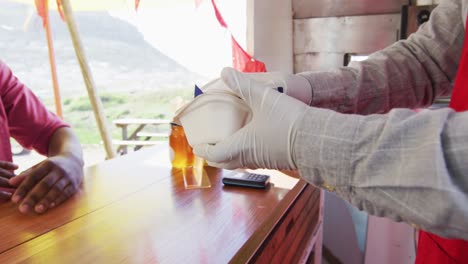 dueño de un camión de comida con guantes pasando el pedido de comida a un cliente afroamericano